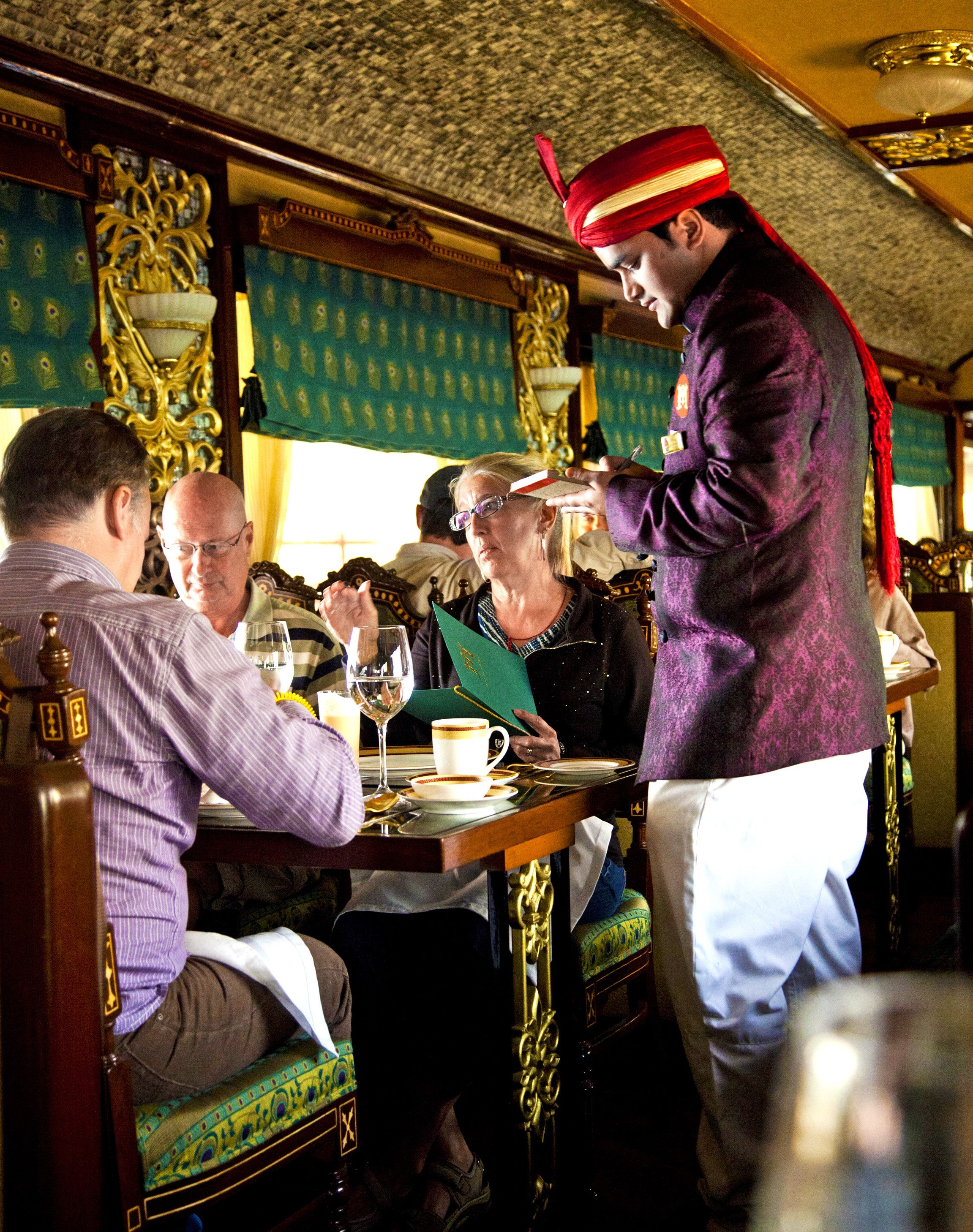 Hovimestari johdattaa matkailijat pöytiin ja tarjoilija ottaa tilaukset ravintolavaunussa.