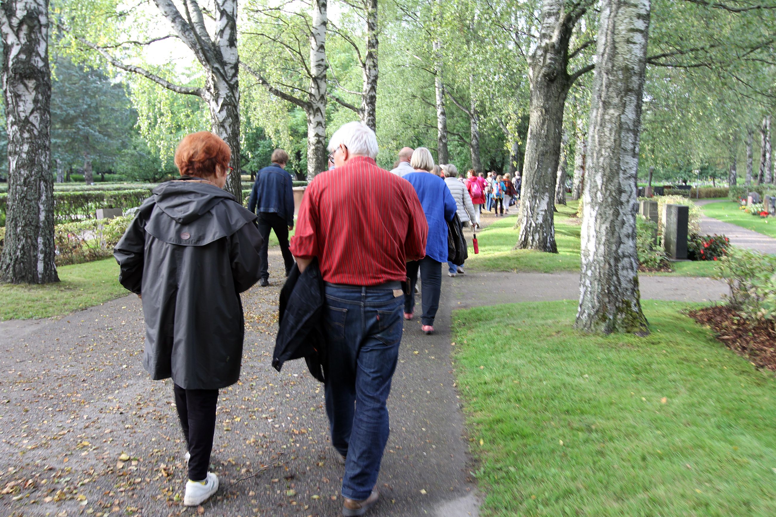 Osallistujajoukko kävelee pappi Risto Alajan perässä Malmin hautausmaalla. 