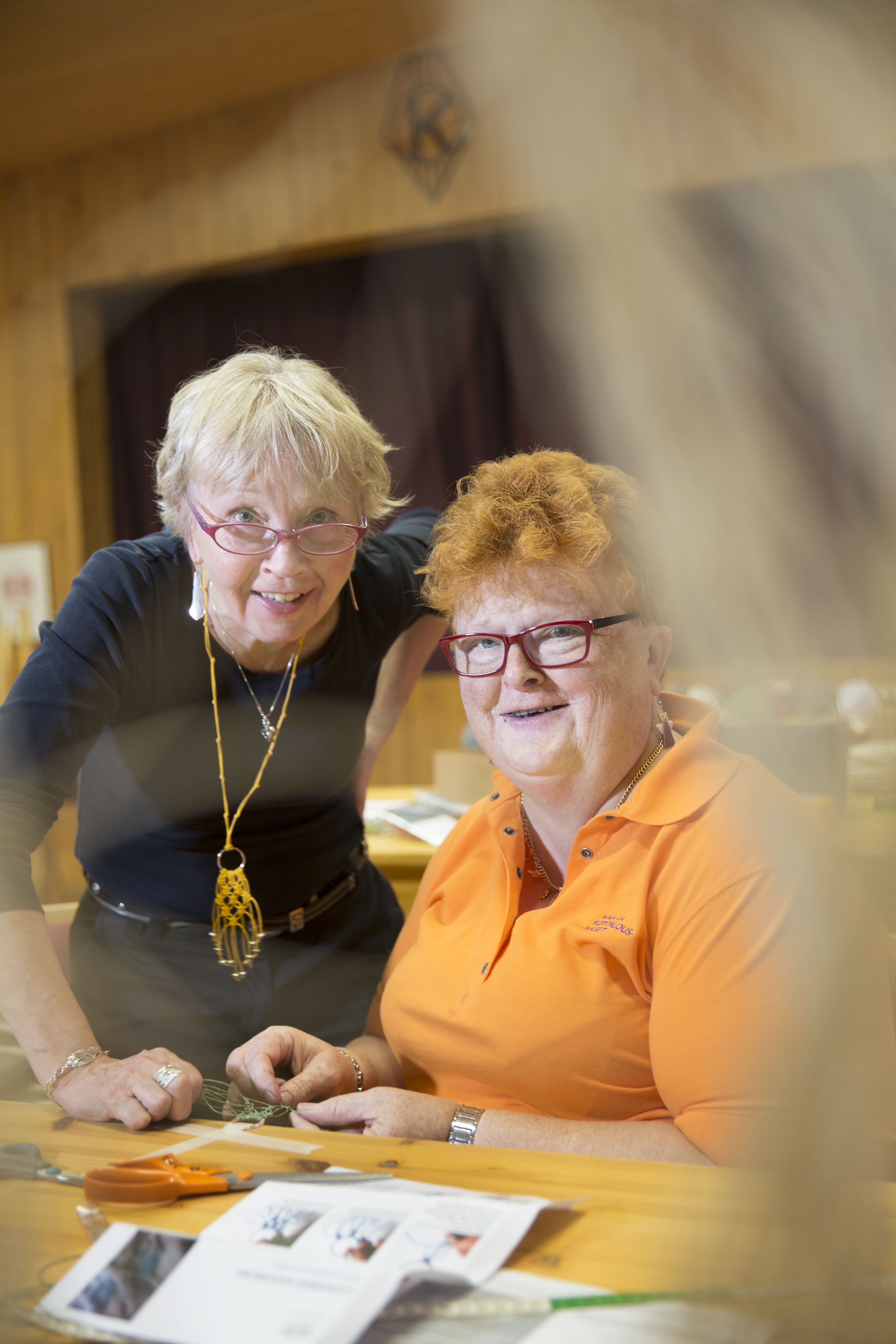 Päivi-opella on kaulassaan makrameekoru. Kurssilainen Päivi Kuronen solmii korua vihreästä paperinarusta.